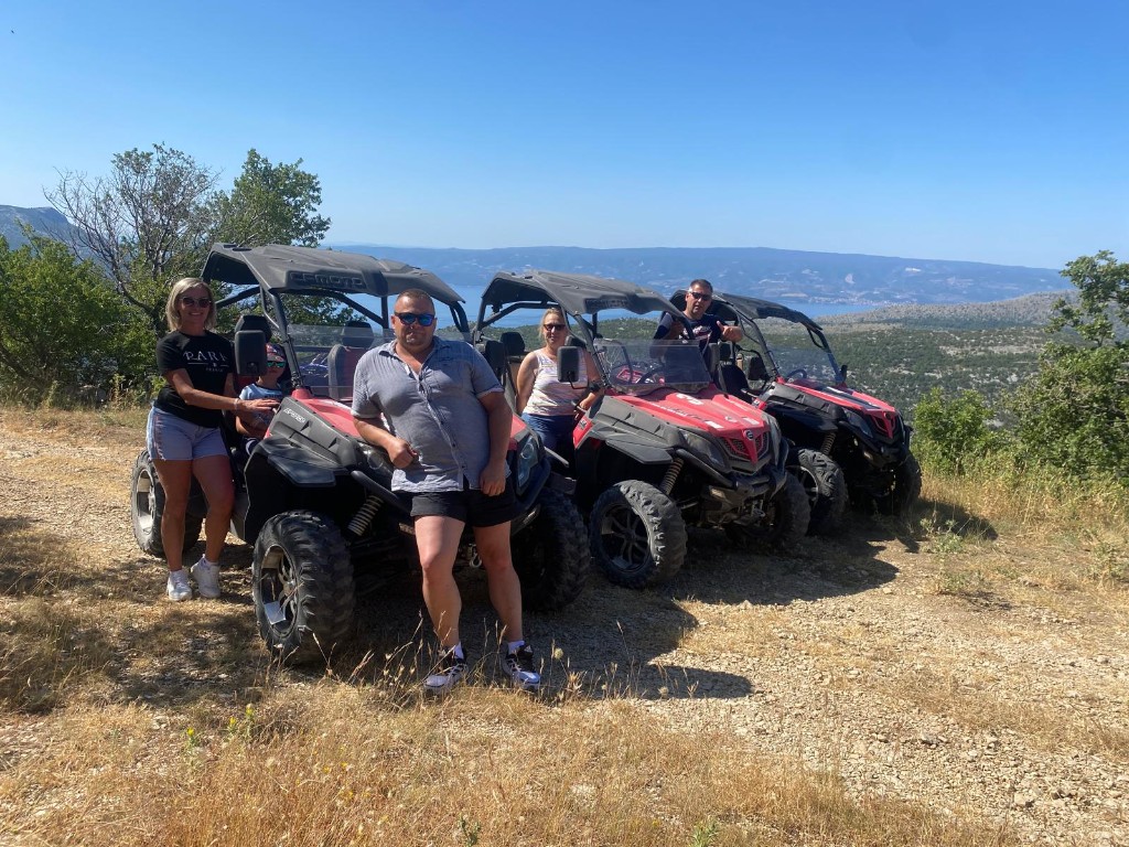 Group with red CFMOTO buggies on a mountain trail above the sea