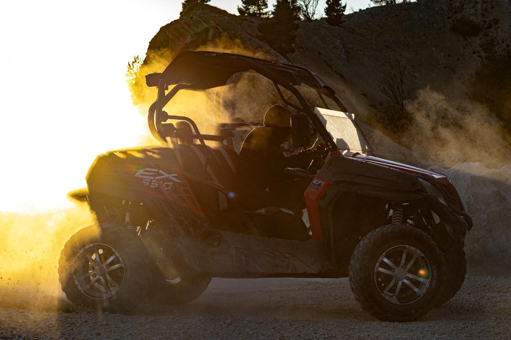 Red and black off-road buggy kicking up dust on a mountain trail during golden sunset light
