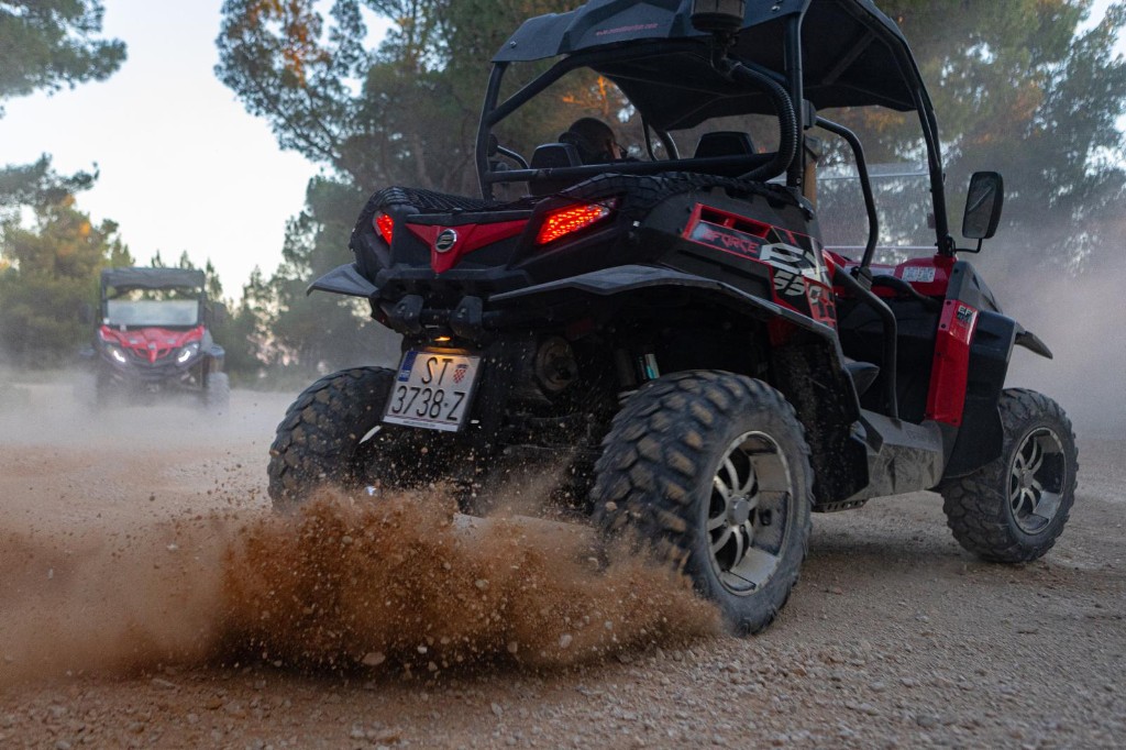 Two red CFMOTO ZFORCE buggies kicking up dust on a pine forest trail near Omiš, Croatia