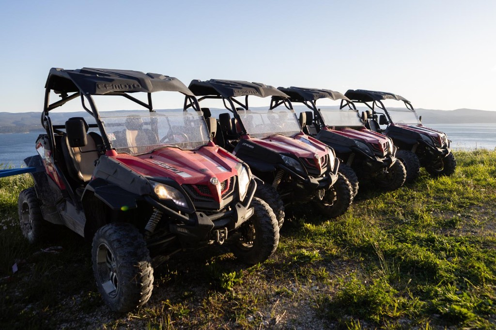 Line of red CFMOTO buggies on a hilltop overlooking the sea at golden hour