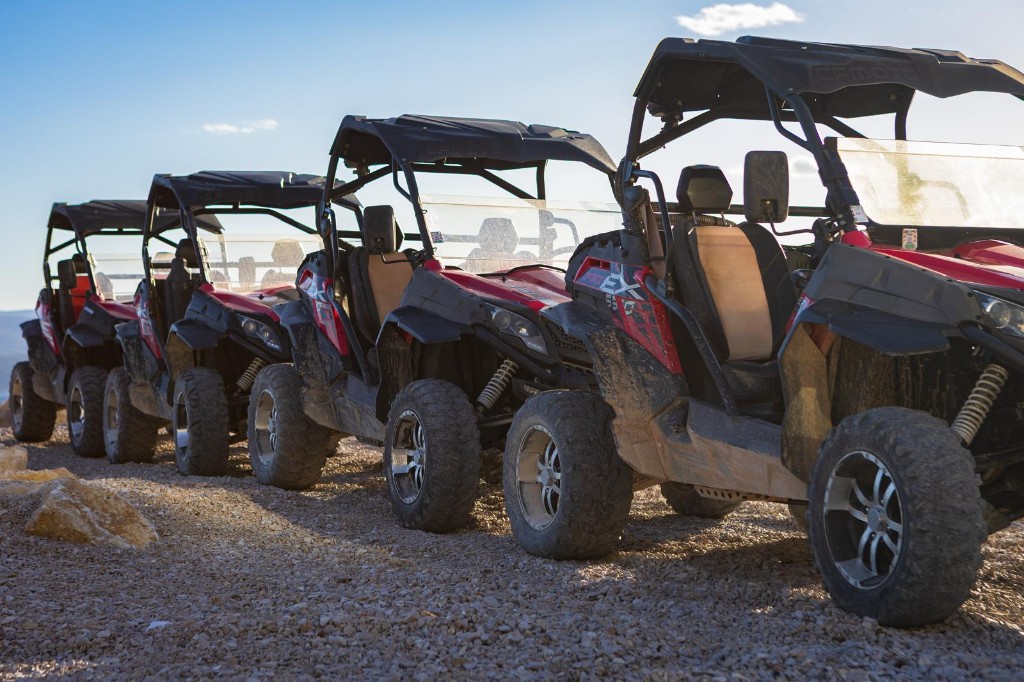 Line of red CFMOTO off-road buggies on a gravel trail under blue sky